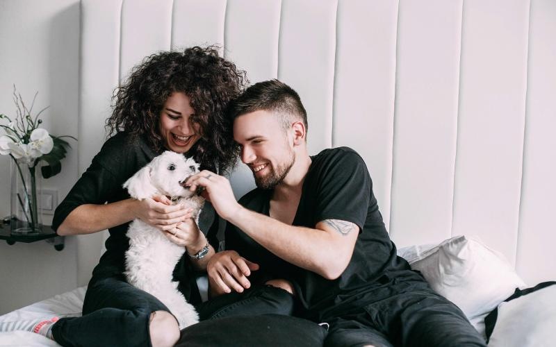 a man and woman sitting on a bed playing with a dog